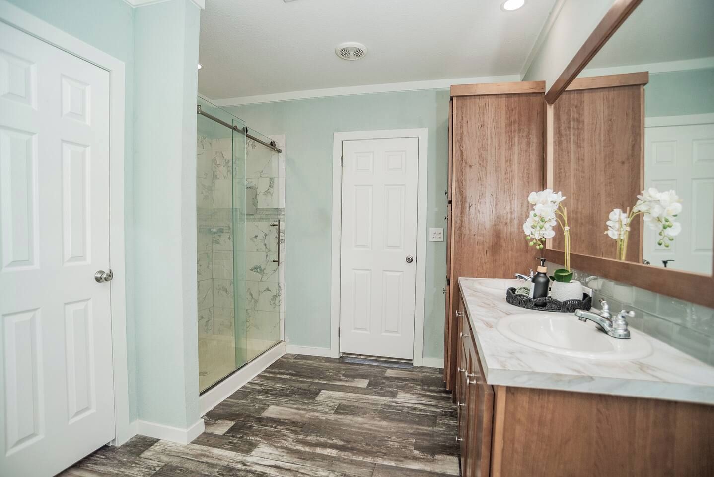 A bathroom with a glass shower, a wooden vanity, and a white door.