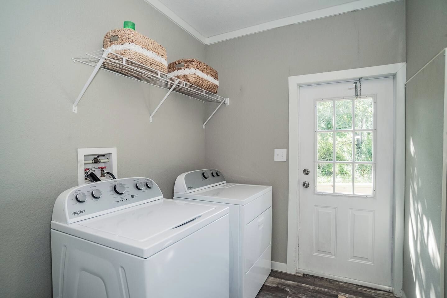 A laundry room with two Whirlpool washers, a white door, and a window.