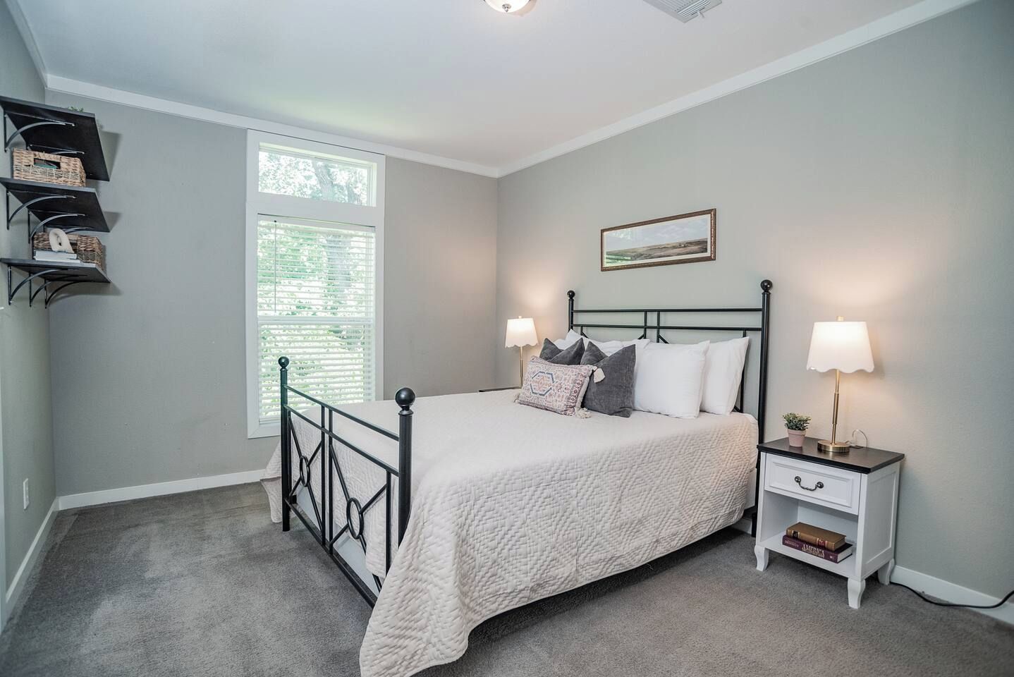 A bedroom with a bed, bedside tables, a window, and a wall-mounted shelf.