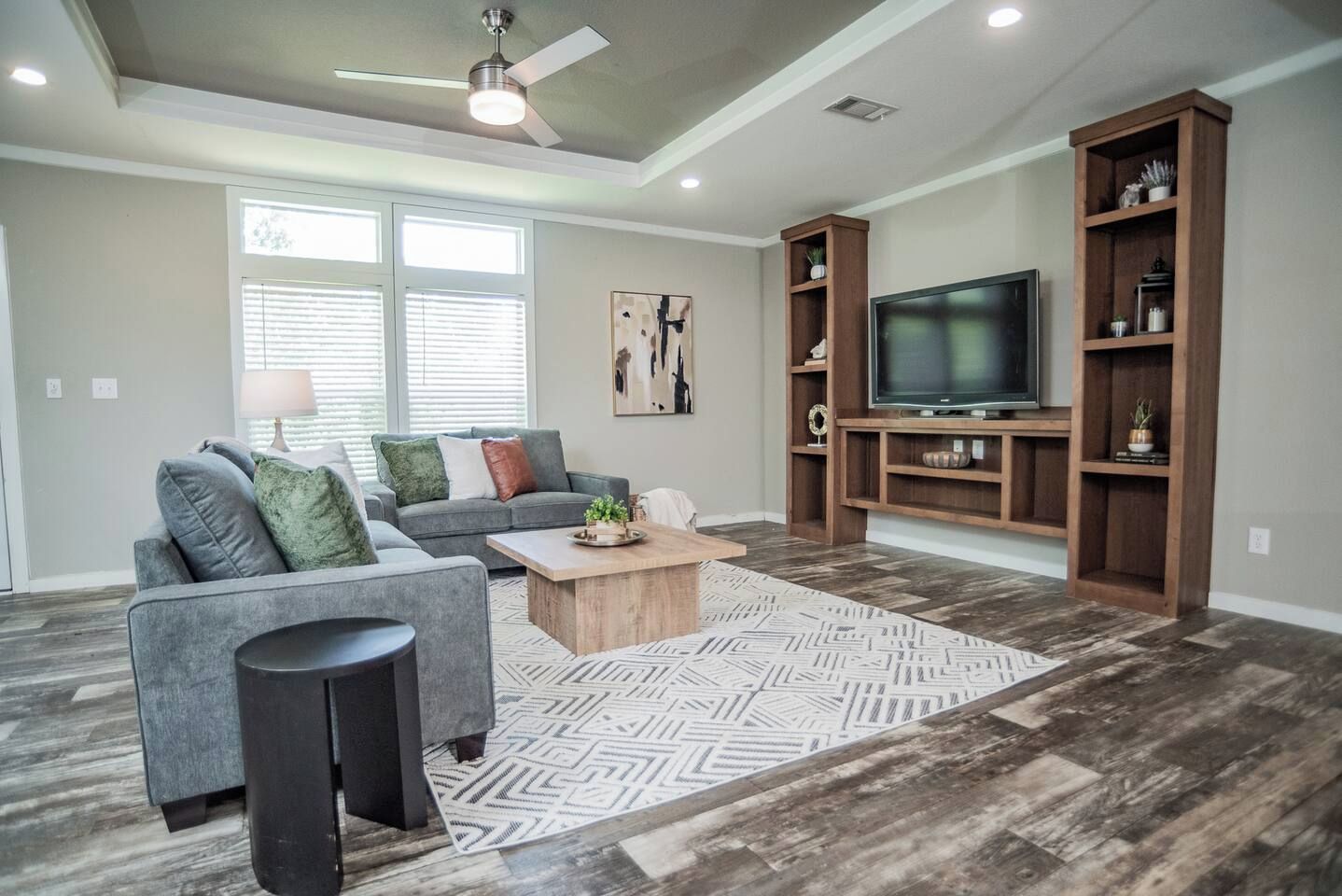 A living room with a gray sectional sofa, a coffee table, a TV on a wooden stand, and a patterned rug.