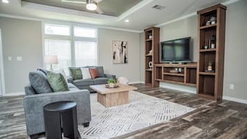 A living room with a gray sectional sofa, a coffee table, a TV on a wooden stand, and a patterned rug.