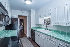 A kitchen with white cabinets, a green tiled backsplash, a stainless steel refrigerator, and a sink with a faucet. - Terminal Wake House-Lake McQueeney (McQueeney)