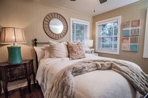 A bedroom with a bed, a round mirror, two windows with blinds, a lamp, and a decorative wall piece. - Terminal Wake House-Lake McQueeney (McQueeney)