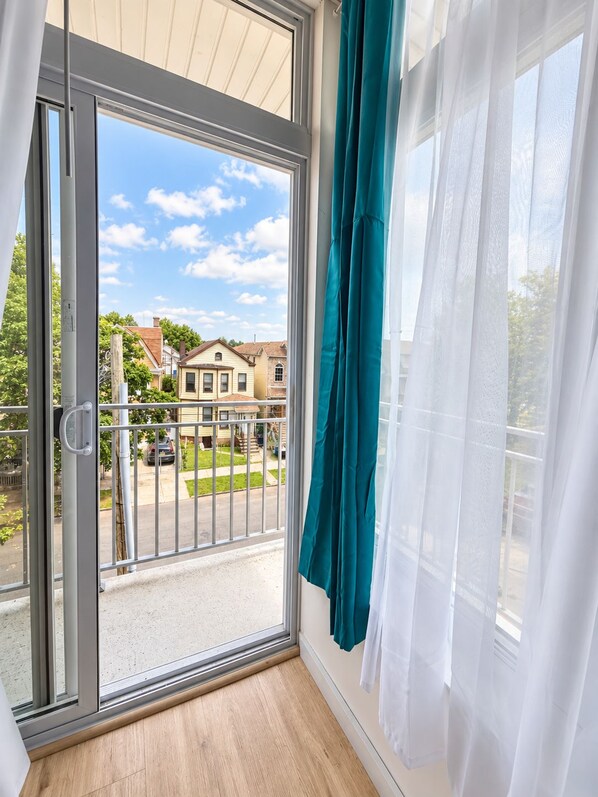 A room with a sliding glass door leading to a balcony, a white curtain, and a view of houses and a street.
