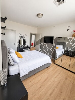 A modern bedroom with a bed, bedside table, mirror, and a TV.