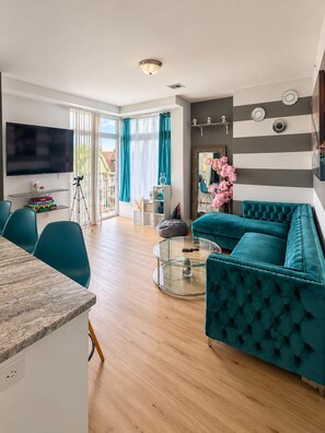 Un salon moderne avec un canapé de couleur turquoise, une table basse en verre et un téléviseur à écran plat.