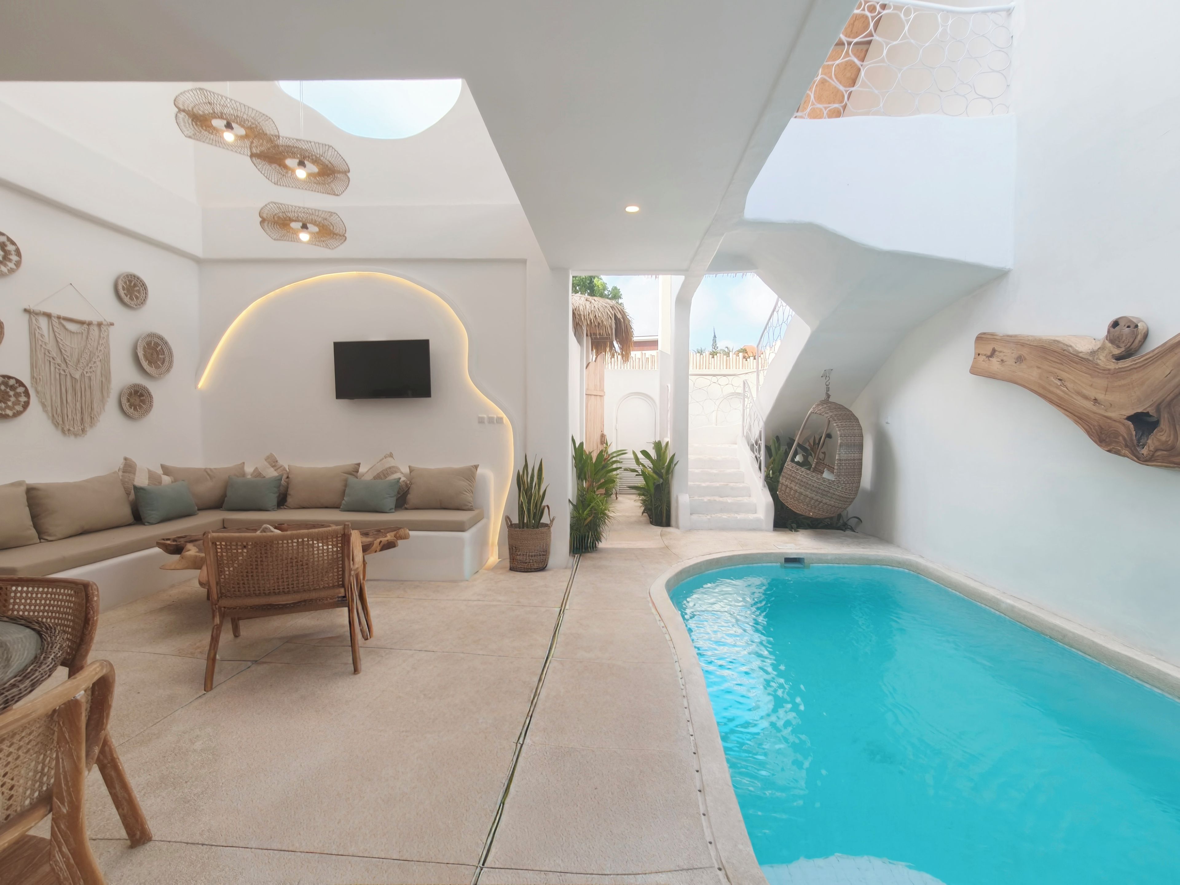 A modern interior with a pool, a sofa, wicker furniture, and a flat-screen TV.
