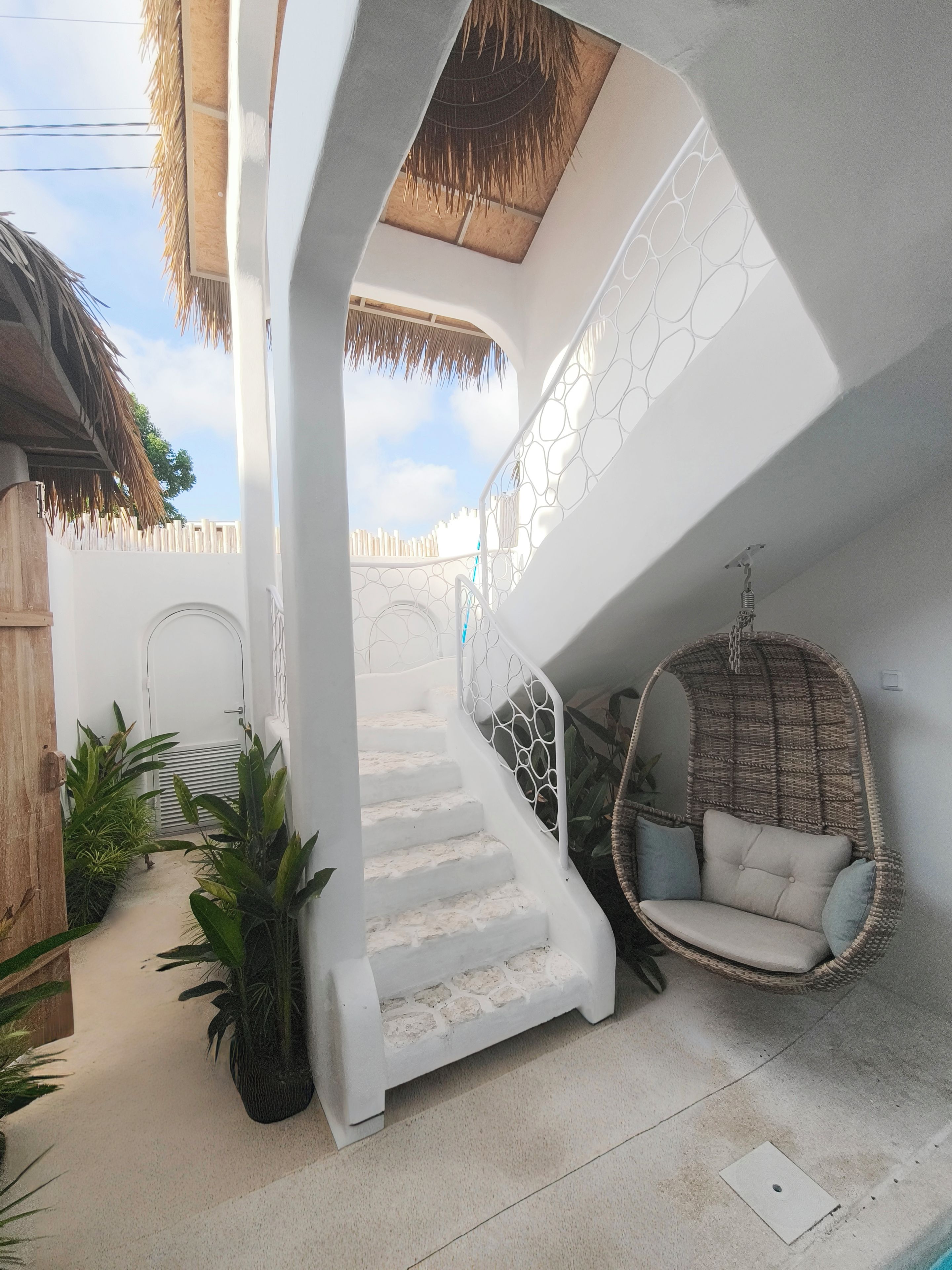 A white staircase leading to a balcony with a hanging chair and potted plants.
