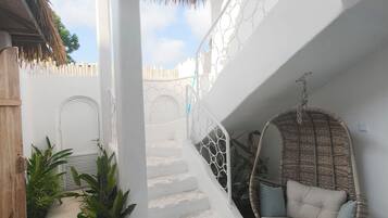 A white staircase leading to a balcony with a hanging chair and potted plants.