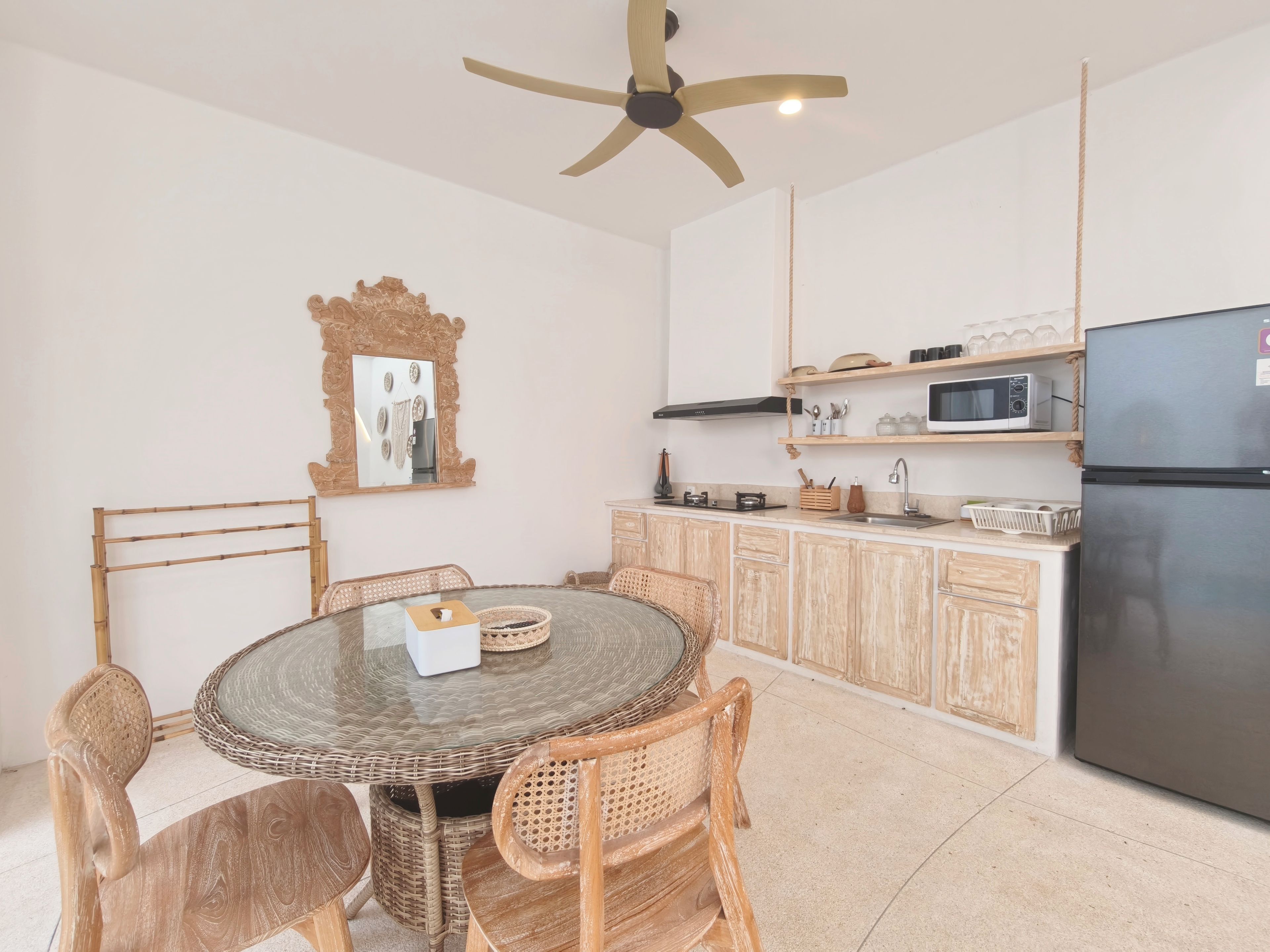 A kitchen with a round dining table, wicker chairs, a microwave, and a refrigerator.