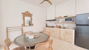 A kitchen with a round dining table, wicker chairs, a microwave, and a refrigerator.