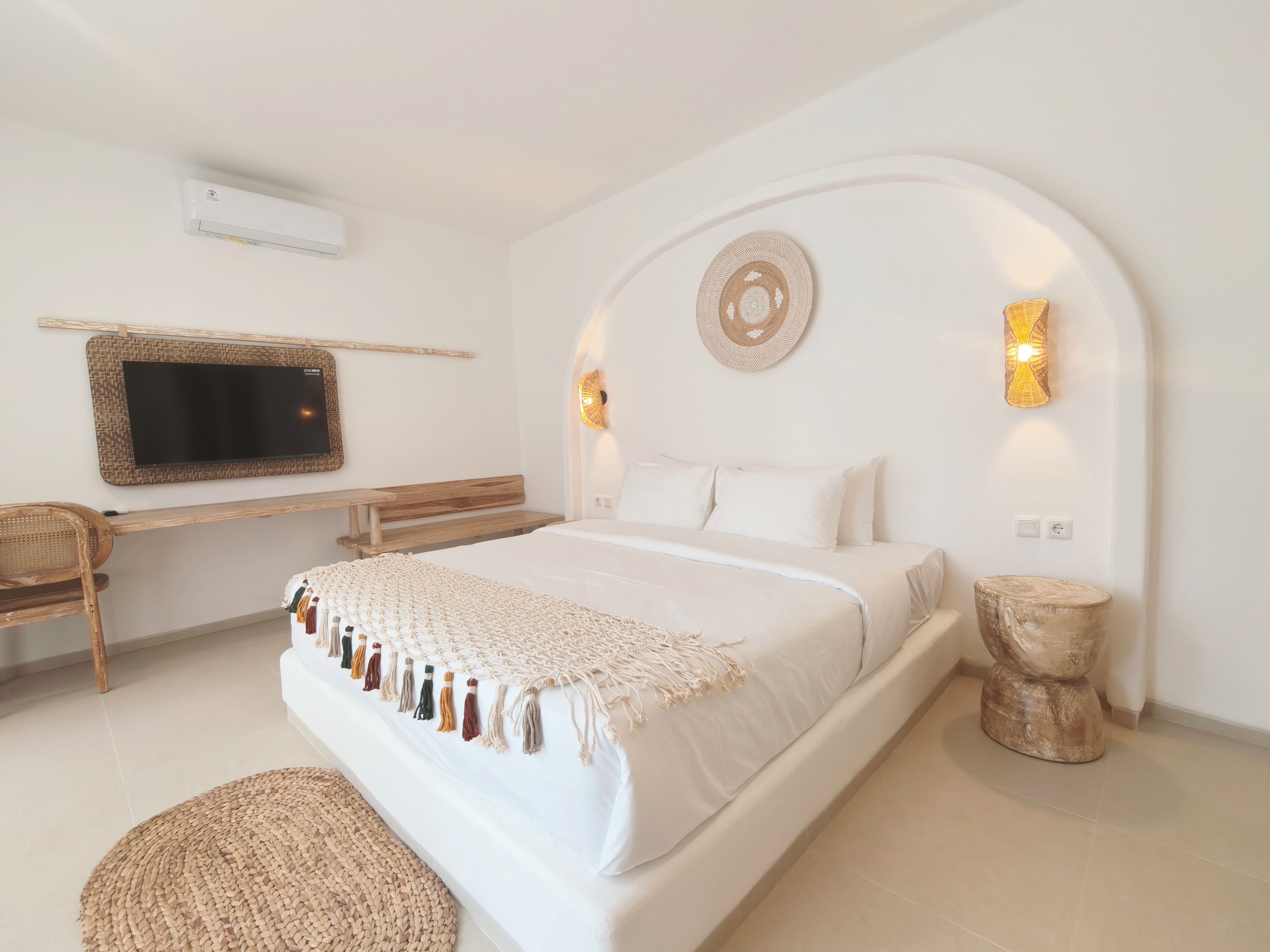 A bedroom with a bed, a desk, a chair, a television, and wall-mounted lights.