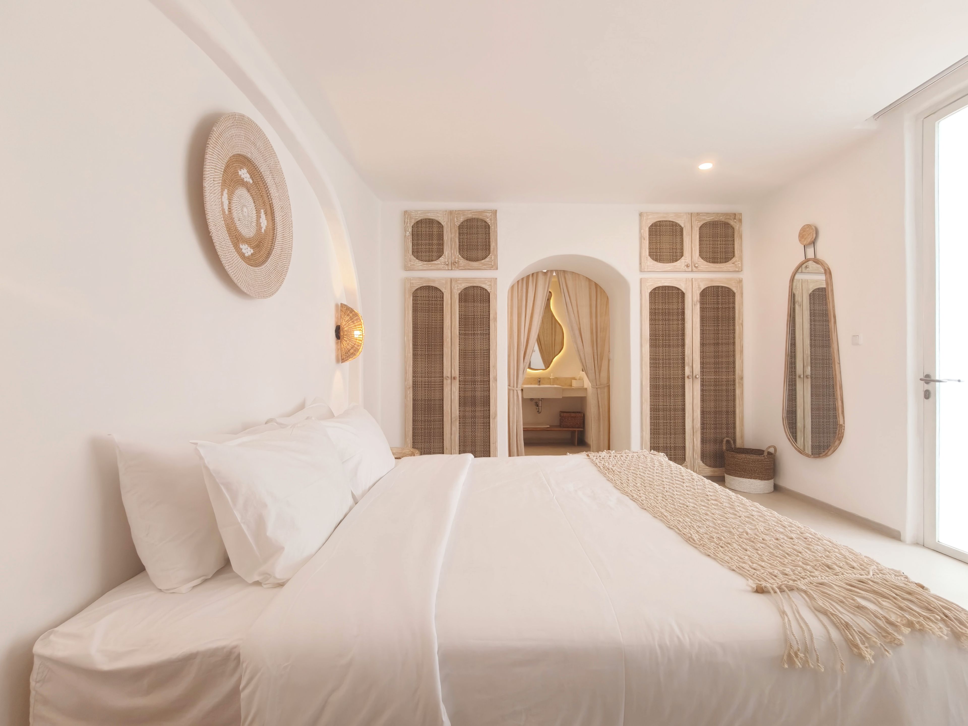 A bedroom with a bed, a wall-mounted lamp, a mirror, and a doorway leading to a bathroom.