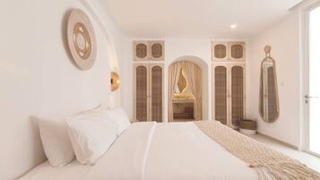 A bedroom with a bed, a wall-mounted lamp, a mirror, and a doorway leading to a bathroom.