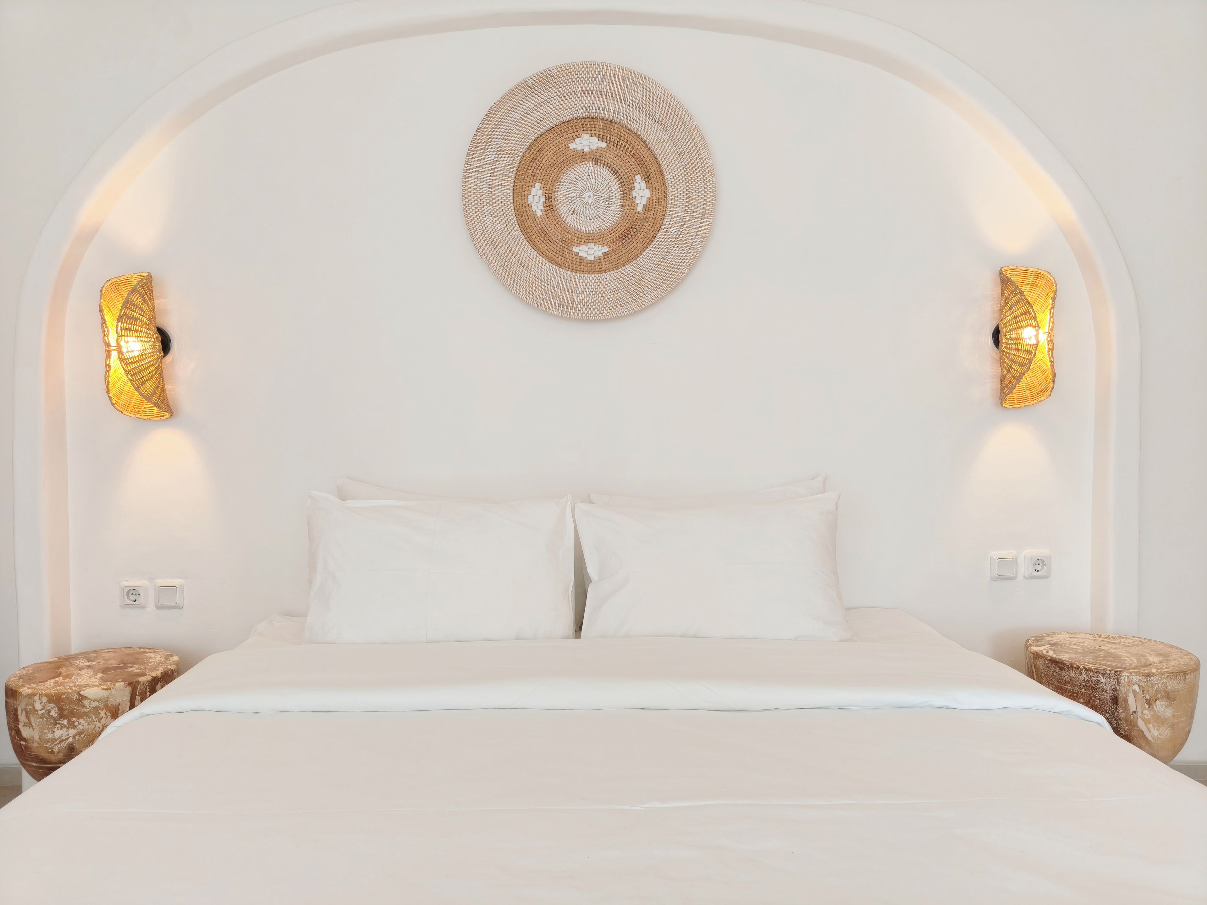 Ein Bett mit weißen Bettwäsche, zwei Wandleuchten und ein gewebtes Wandbild.