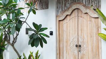 A wooden door with intricate carvings, a thatched roof, and lush greenery.