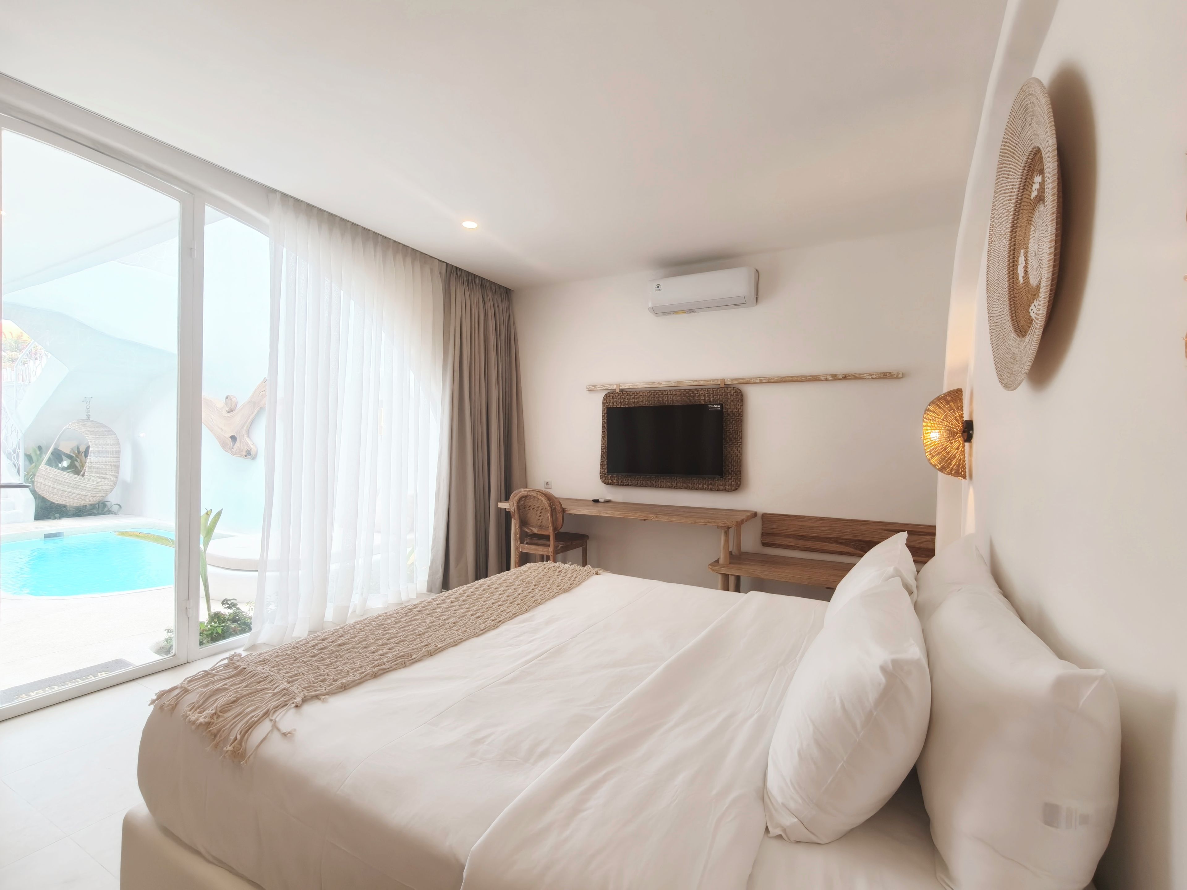 Quarto de hotel com cama, escrivaninha, televisão e vista para uma piscina.