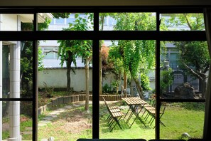 Vista a través de una ventana de un patio con una mesa y sillas de madera, un camino de piedra y una cerca.