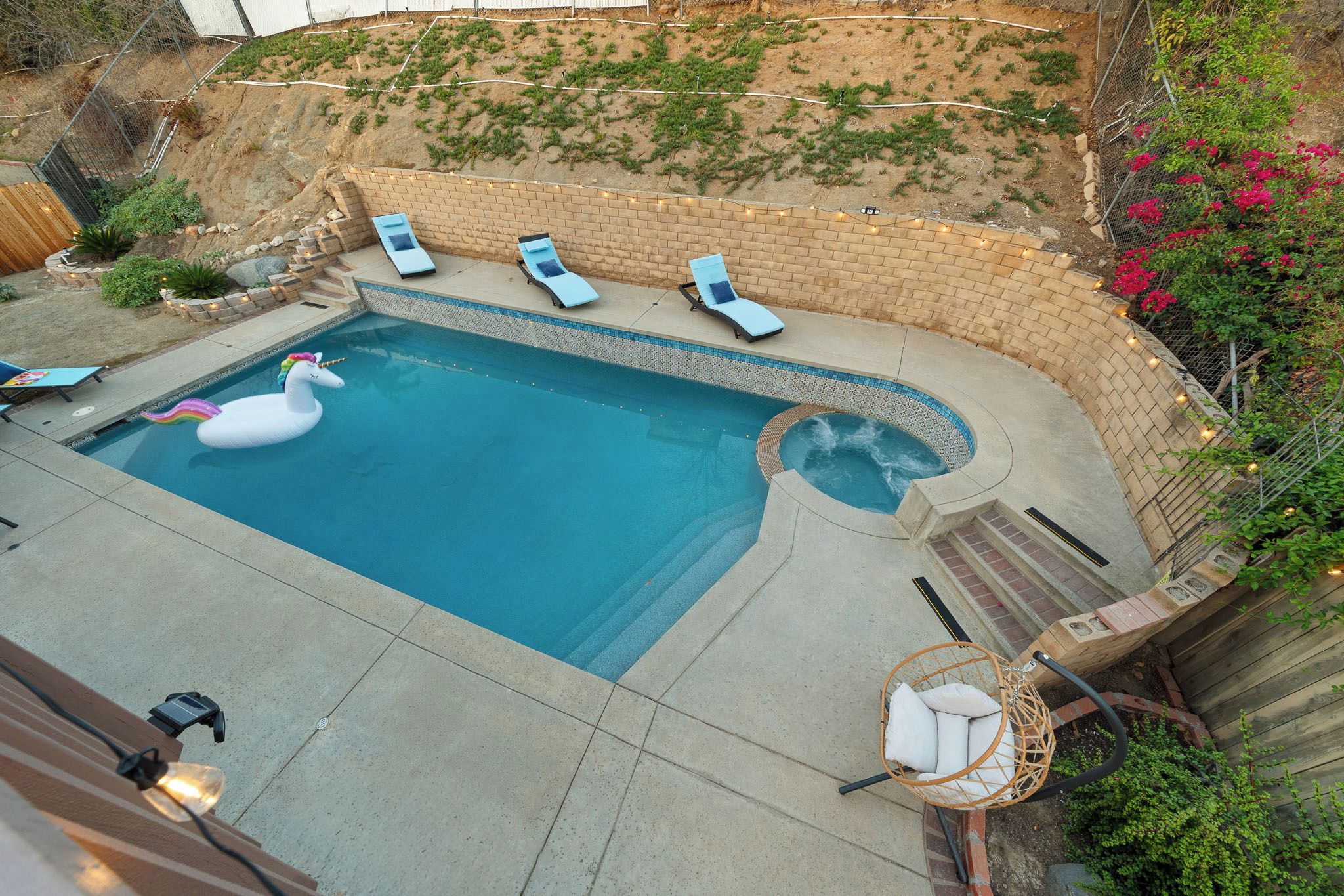 A backyard swimming pool with a hot tub, lounge chairs, and a decorative unicorn float.