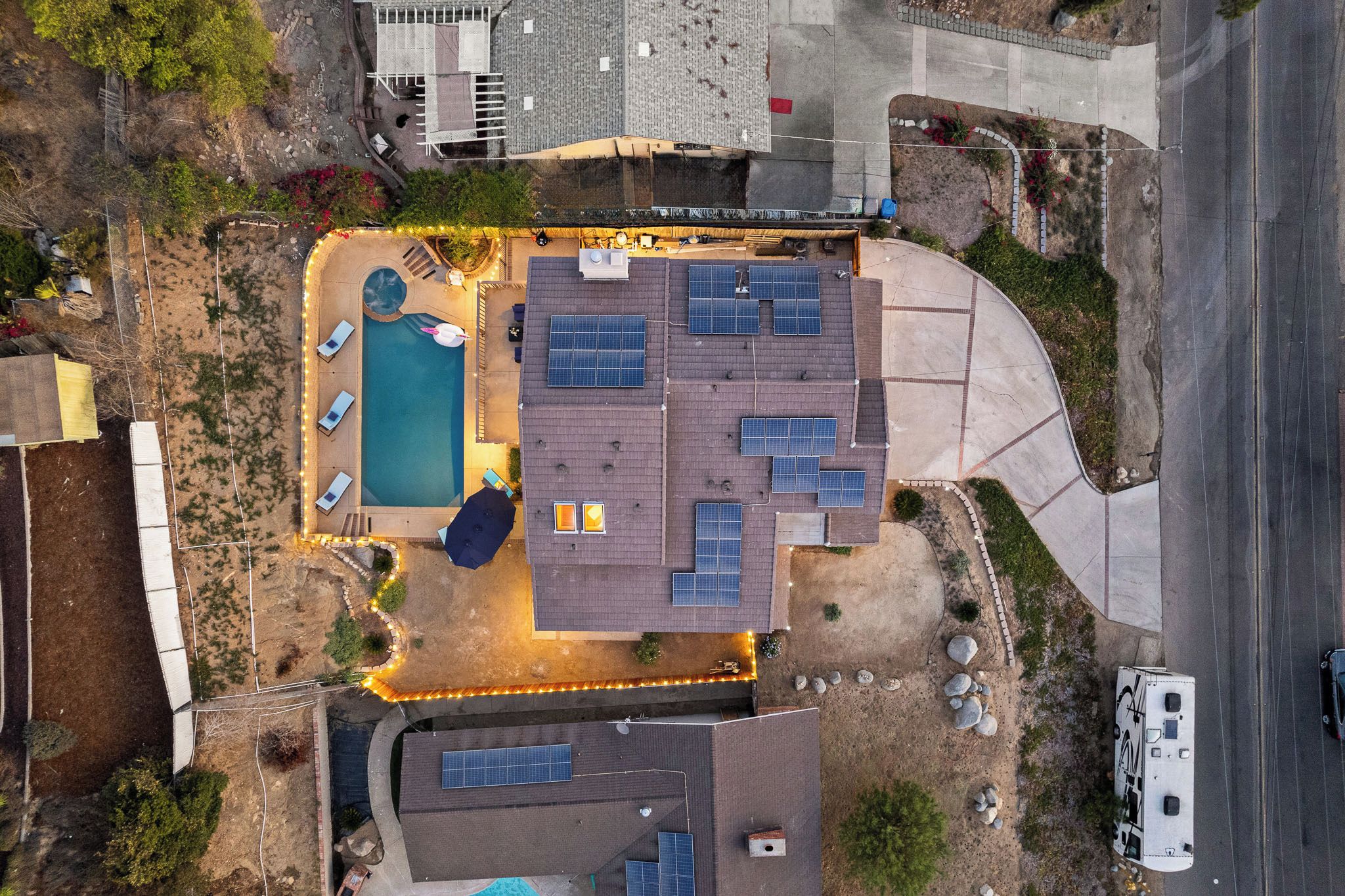 An aerial view of a residential property with a swimming pool, solar panels, and a curved driveway.