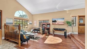 A spacious living room with a pool table, comfortable seating, and large windows.