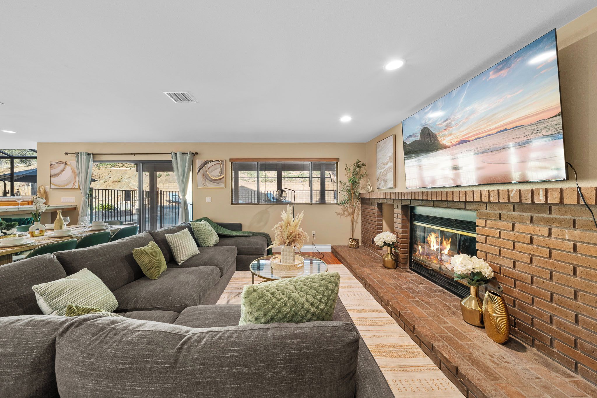 A living room with a sectional sofa, a glass coffee table, a fireplace, and a large painting above it.