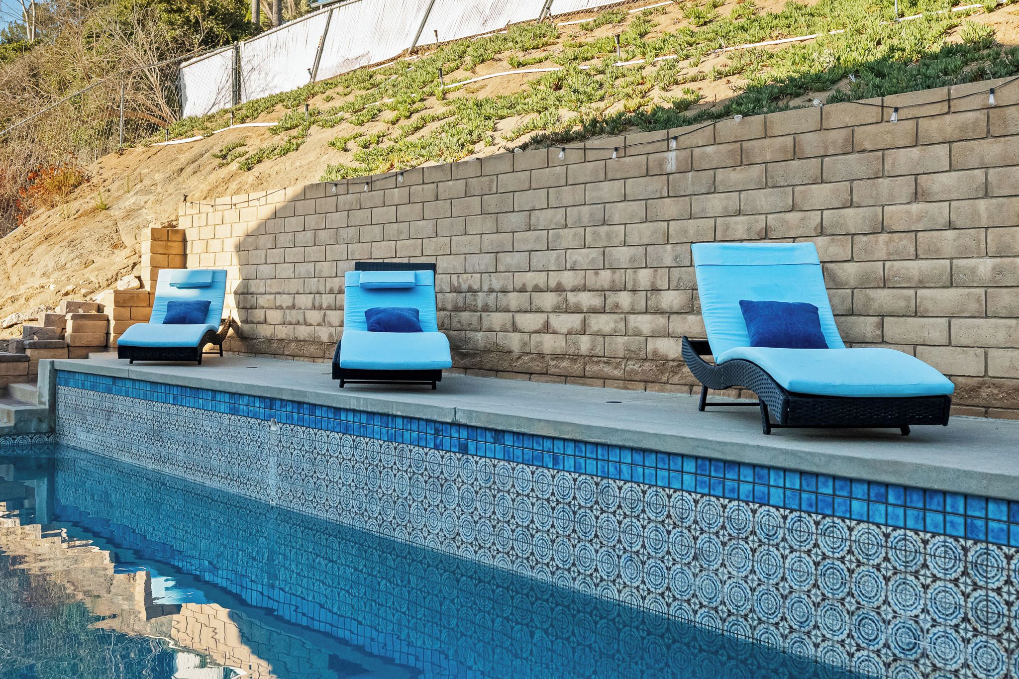 A poolside area with three lounge chairs and a tiled pool.