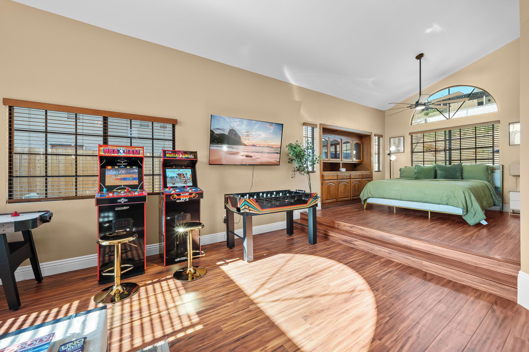 A room with a bed, a foosball table, two arcade machines, and a television.