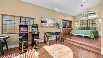 A room with a bed, a foosball table, two arcade machines, and a television.