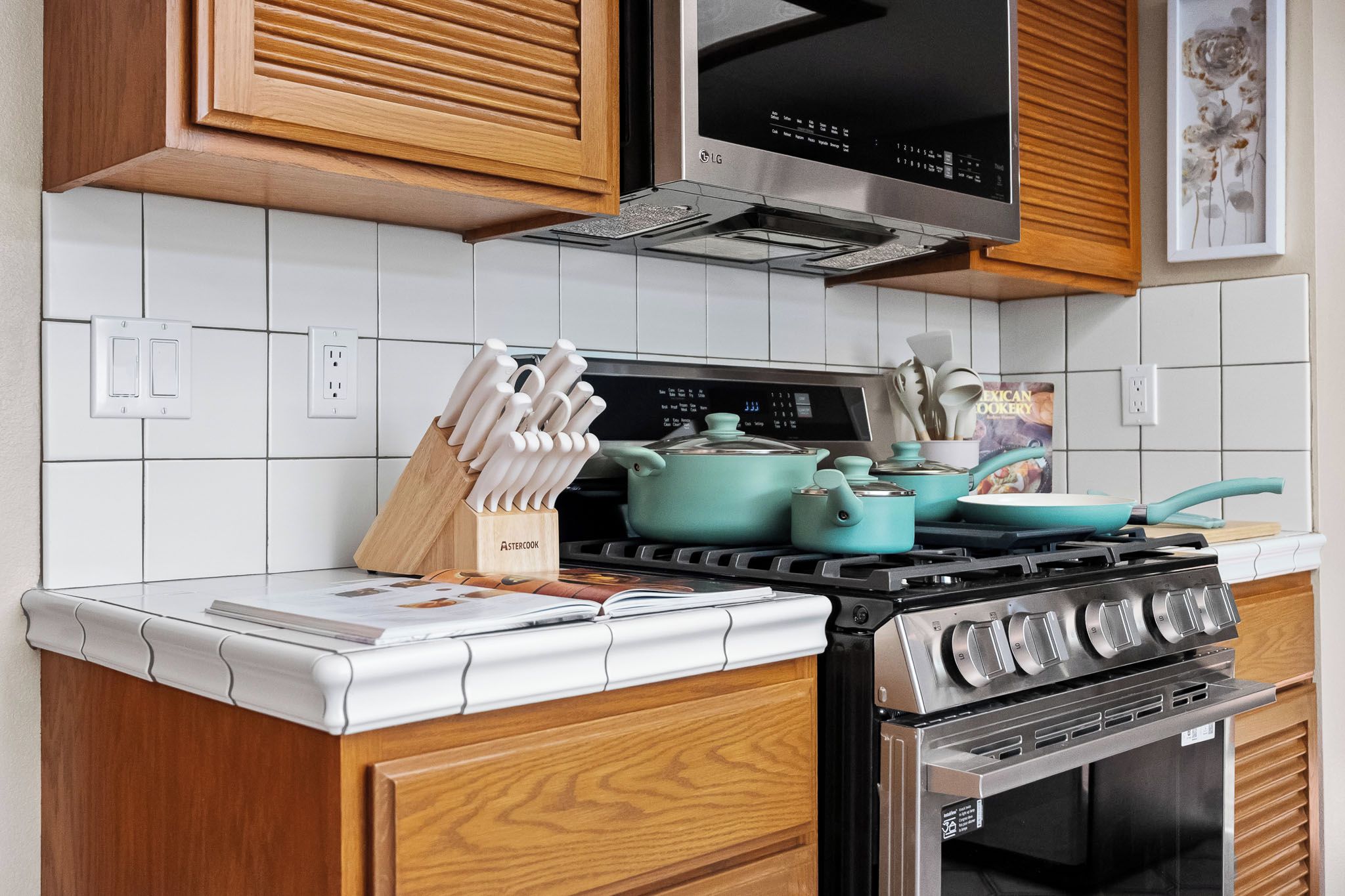 A kitchen with a stove, pots, a knife block, and a cookbook on the counter.