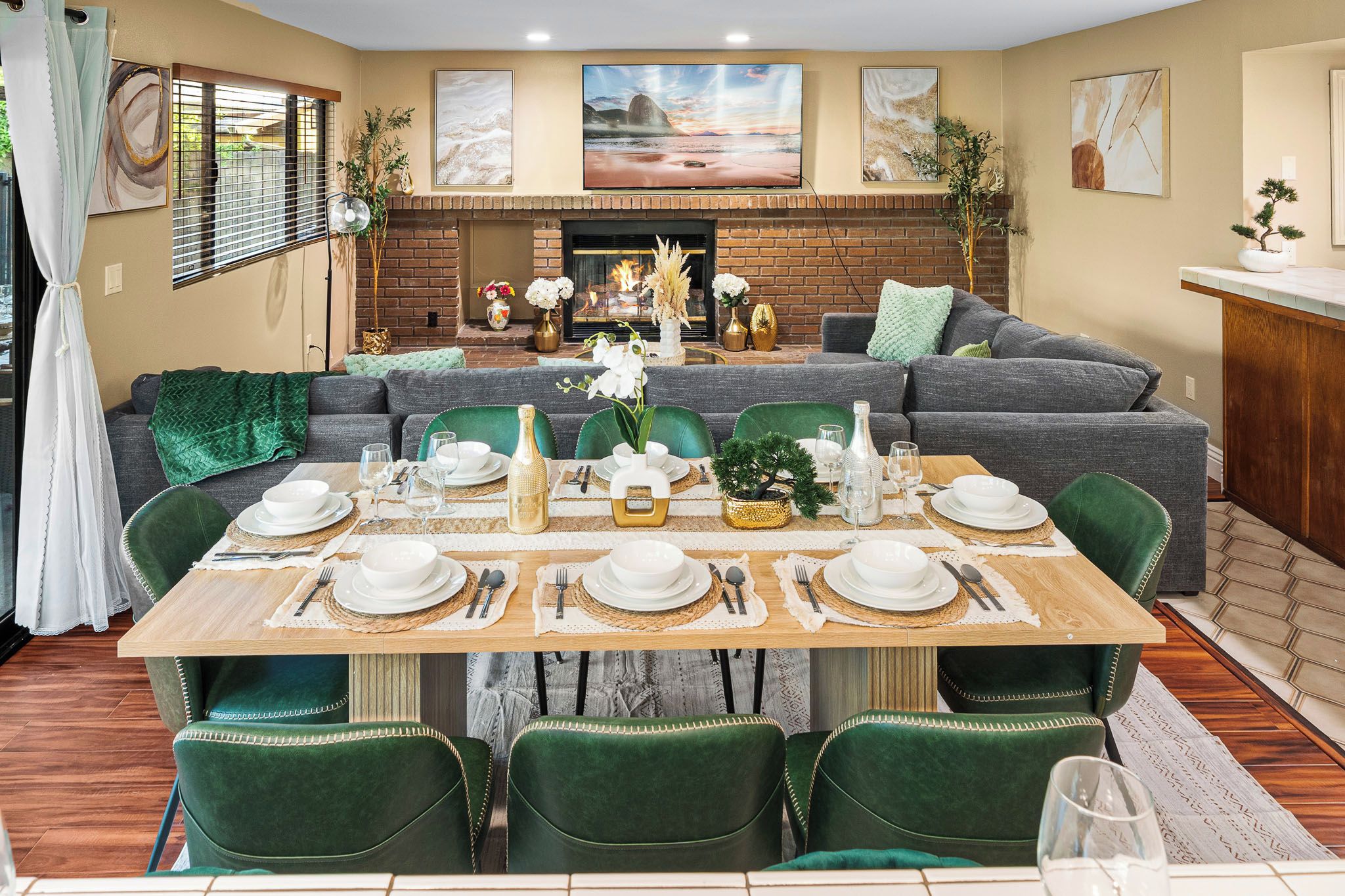 A dining area with a brick fireplace, green upholstered chairs, and a table set for six.