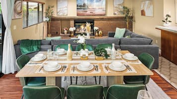 A dining area with a brick fireplace, green upholstered chairs, and a table set for six.