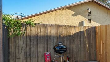 A backyard with a wooden fence, a barbecue grill, and a bag of charcoal.