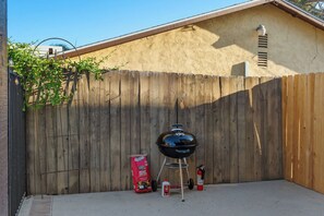 Un patio trasero con cercado de madera, una parrilla y un saco de carbón.