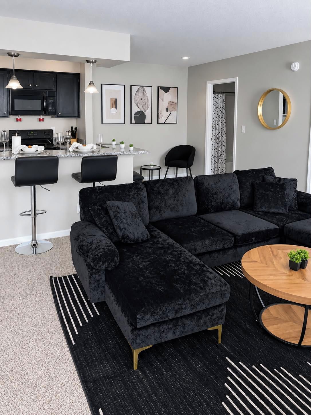 A modern living room with a sectional sofa, a round coffee table, and a kitchen area with a microwave and dining setup.