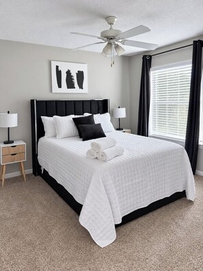 A bedroom with a bed, two bedside tables, a ceiling fan, a window with curtains, and a wall-mounted artwork. - 3 mins from Arsenal/Bridge Street. (Huntsville)