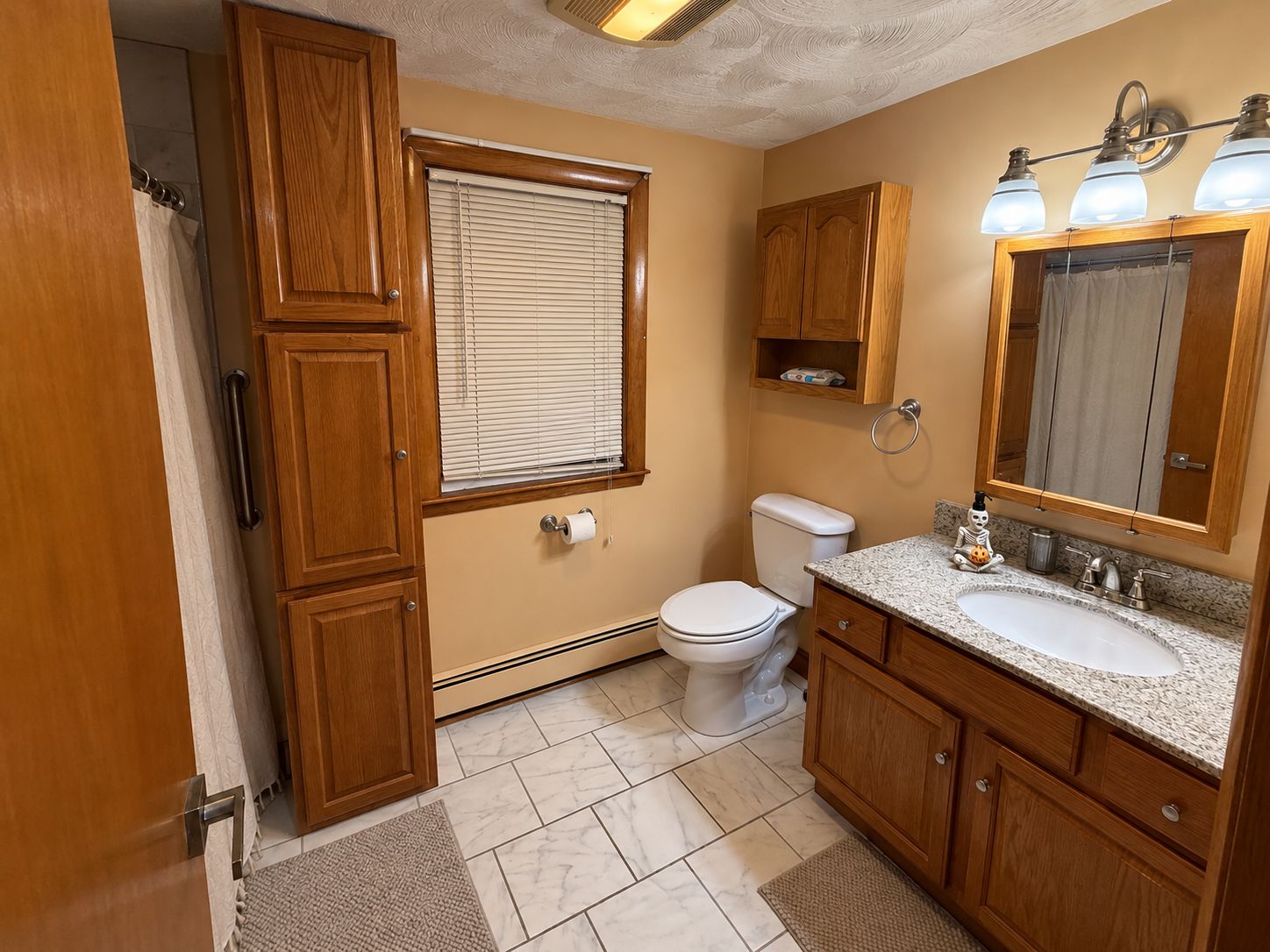 Un baño con armarios de madera, inodoro, lavamanos y ventana con persianas.