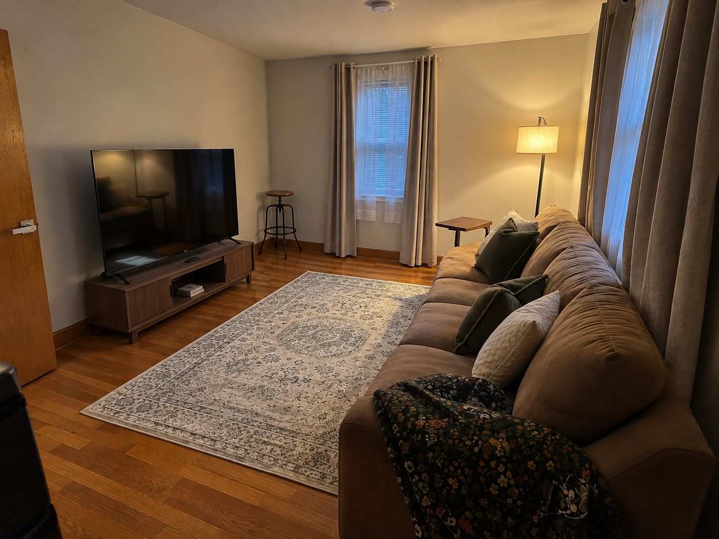 Una sala de estar con un televisor de pantalla plana, un sofá, un tapete estampado y una lámpara.