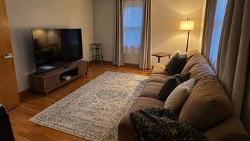 Una sala de estar con un televisor de pantalla plana, un sofá, un tapete estampado y una lámpara.
