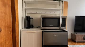 Een kleine keuken met een magnetron, koelkast en koffiezetapparaat op een wit aanrecht.