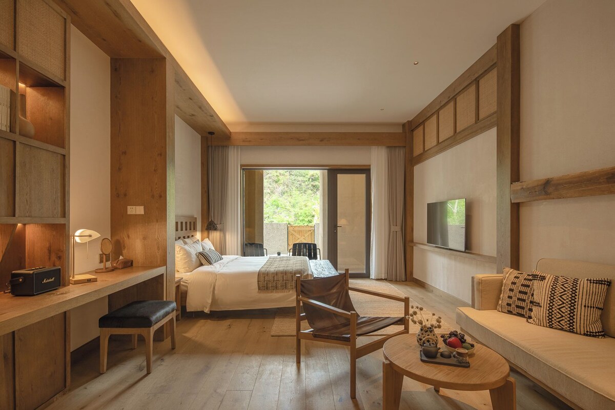 Habitación de hotel con una cama, un escritorio con lámpara, un sofá, un televisor y vistas a zonas verdes.