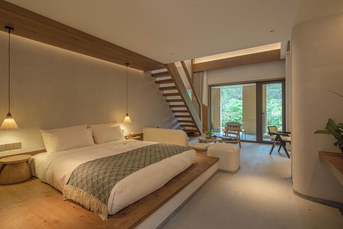 Un dormitorio moderno con una cama grande, una escalera de madera y vistas al exterior.
