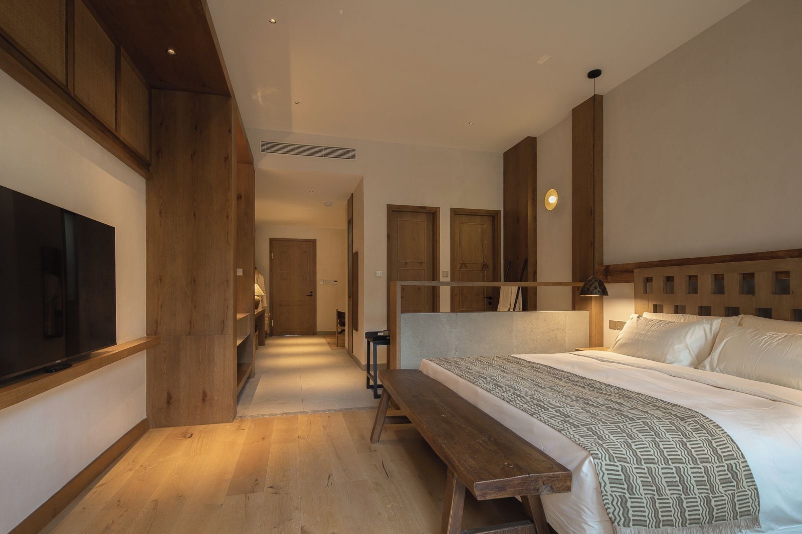 A hotel room with a bed, a bench, a TV, and wooden paneling.