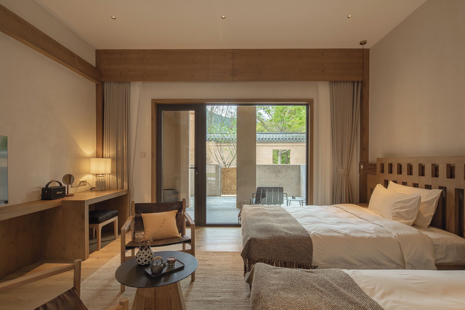 A hotel room with a bed, a desk, a chair, a table, and a view of the outdoors.