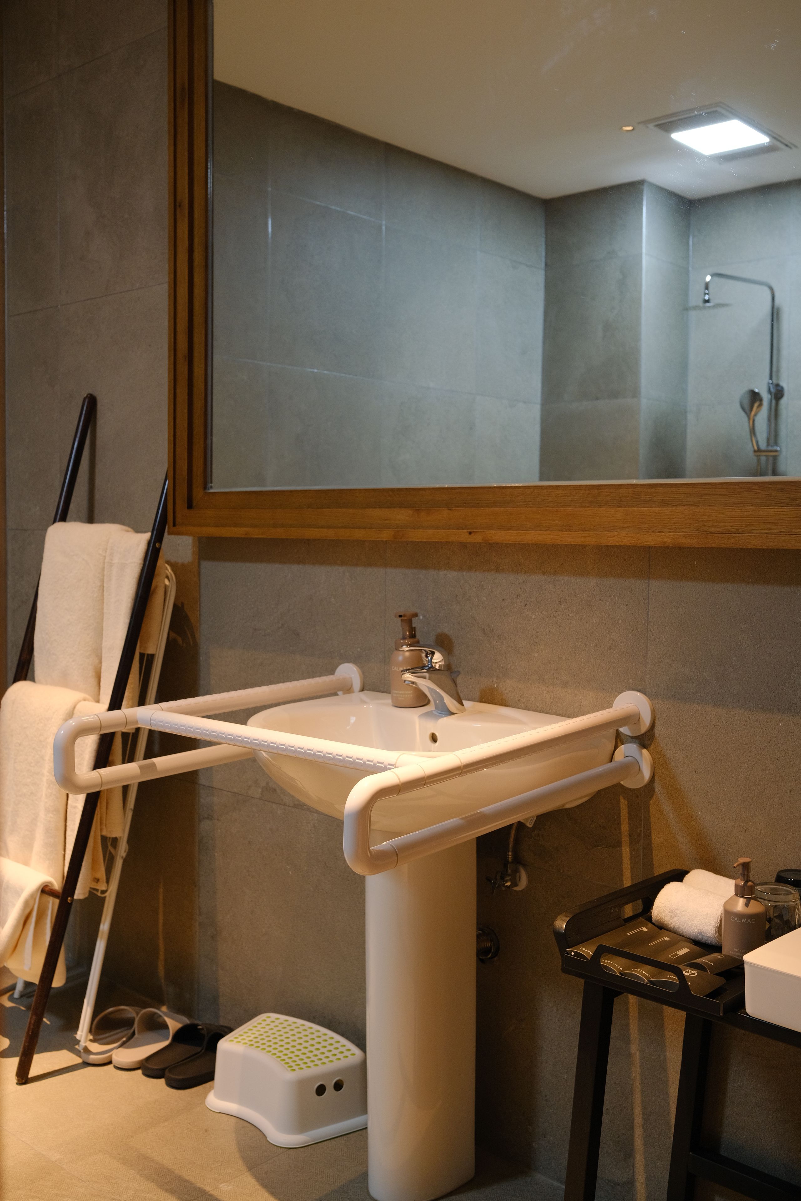 Un baño con un lavamanos blanco, un espejo encima y una zona de ducha al fondo.
