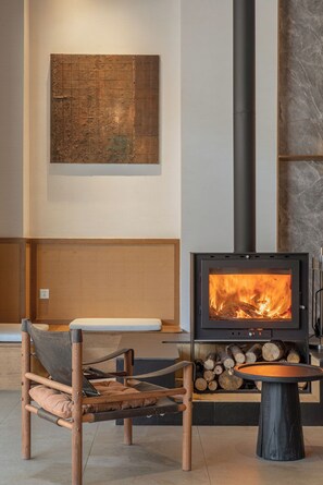 A modern interior with a wood-burning stove, a cushioned chair, and a wall-mounted artwork.