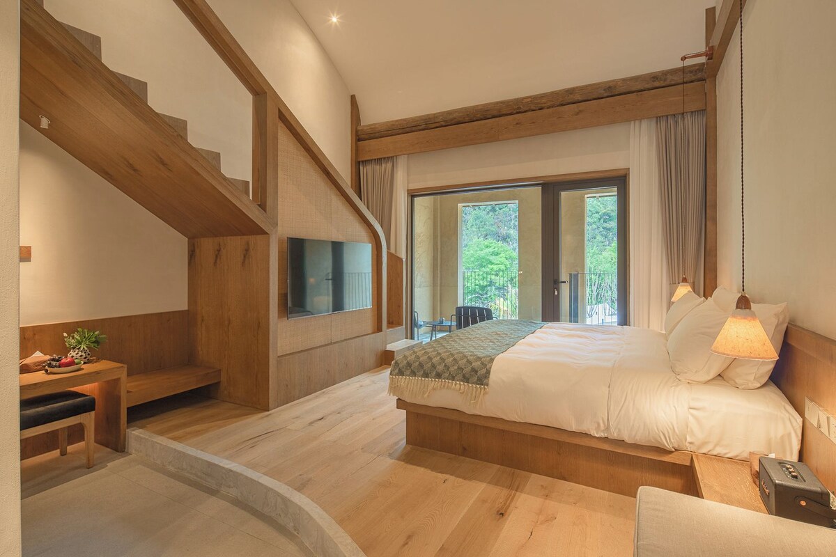 Un dormitorio con una cama grande, un televisor montado en la pared, una escalera y un balcón con vistas a la vegetación.