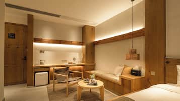 Quarto de hotel com cama, escrivaninha, cadeira, mesinha e luminária pendente.