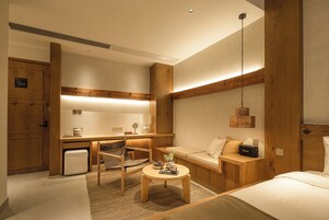Quarto de hotel com cama, escrivaninha, cadeira, mesinha e luminária pendente.