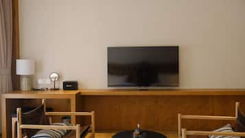 Sala de estar com televisão de tela plana na parede, móveis de madeira, uma mesinha com um objeto decorativo e uma luminária em um criado-mudo.